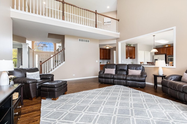 living area featuring baseboards, a high ceiling, dark wood-style flooring, and visible vents