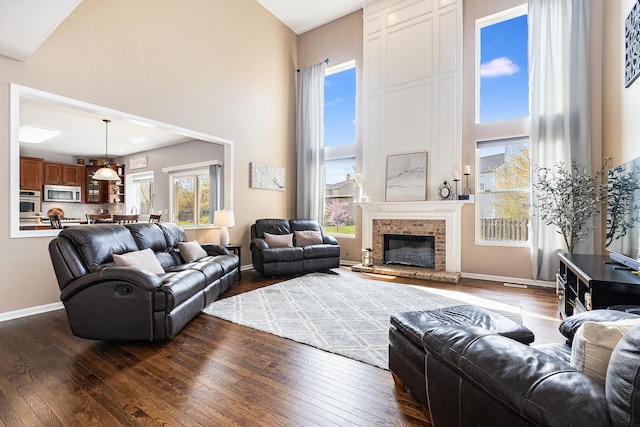 living area featuring baseboards, a high ceiling, dark wood-style floors, and a fireplace