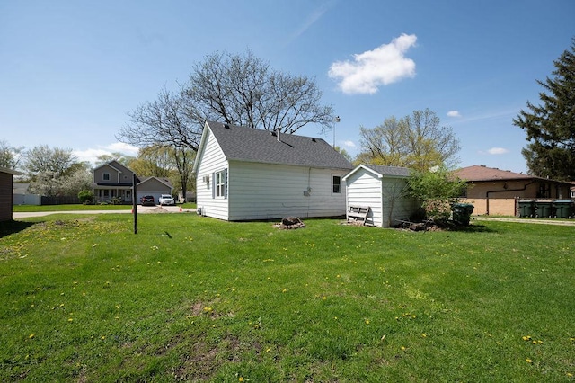 exterior space featuring a storage shed, roof with shingles, a yard, and an outbuilding