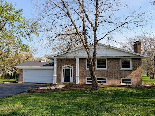 split foyer home with a chimney, brick siding, aphalt driveway, a front yard, and an attached garage