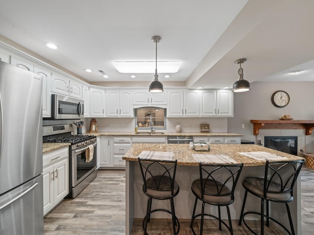 kitchen featuring appliances with stainless steel finishes, a kitchen island, light wood finished floors, a sink, and a kitchen breakfast bar