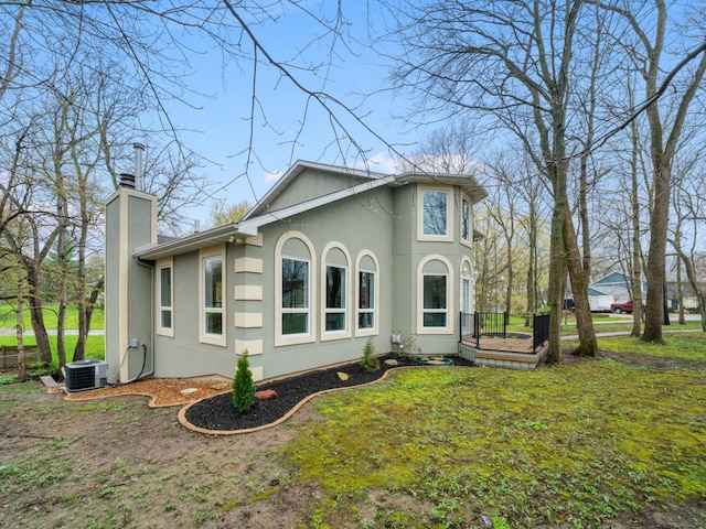 rear view of property featuring a chimney, central AC unit, and stucco siding