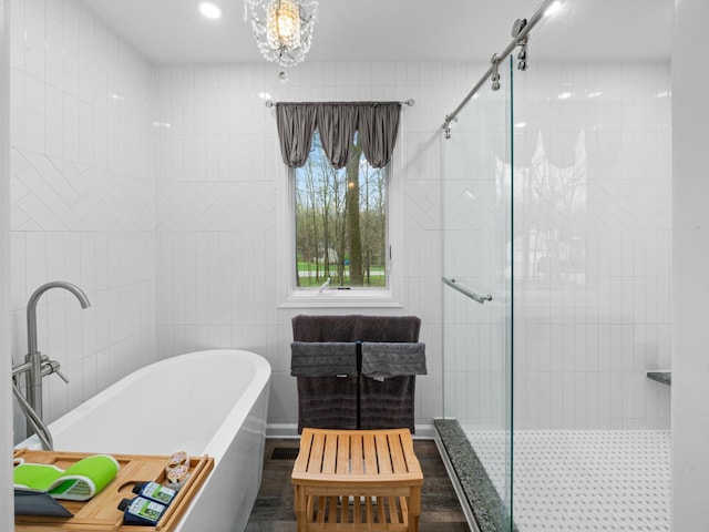 bathroom featuring wood finished floors, a chandelier, a shower stall, and a soaking tub