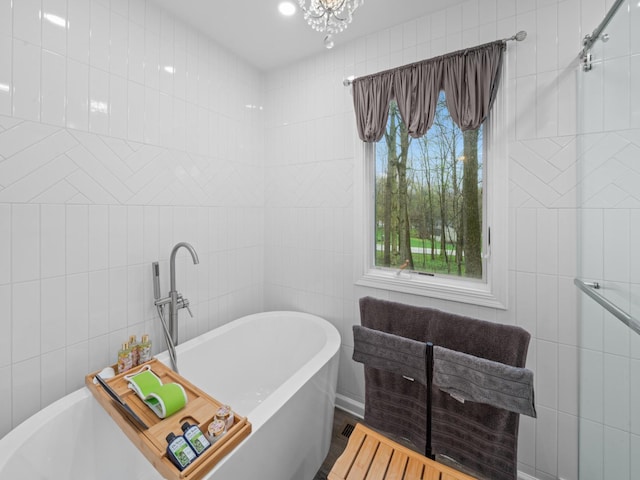 full bath with a chandelier, a freestanding bath, and tile walls