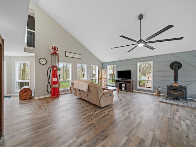 living area featuring wood finished floors, baseboards, high vaulted ceiling, a ceiling fan, and a wood stove
