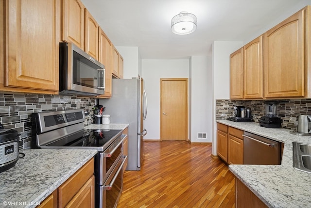 kitchen with visible vents, light stone countertops, light wood finished floors, backsplash, and stainless steel appliances