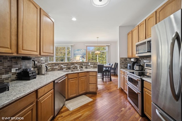 kitchen with appliances with stainless steel finishes, a sink, a peninsula, tasteful backsplash, and hardwood / wood-style flooring
