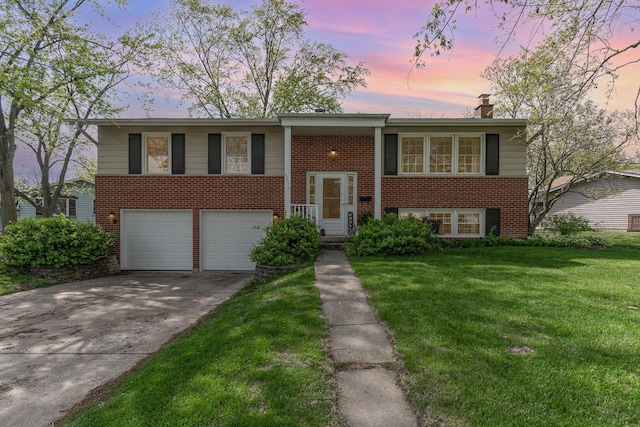 raised ranch featuring a chimney, brick siding, a front lawn, concrete driveway, and an attached garage
