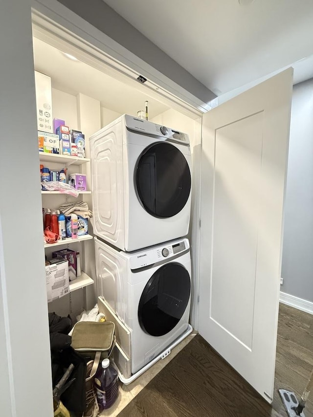 clothes washing area with stacked washer / drying machine, dark wood-style flooring, and laundry area