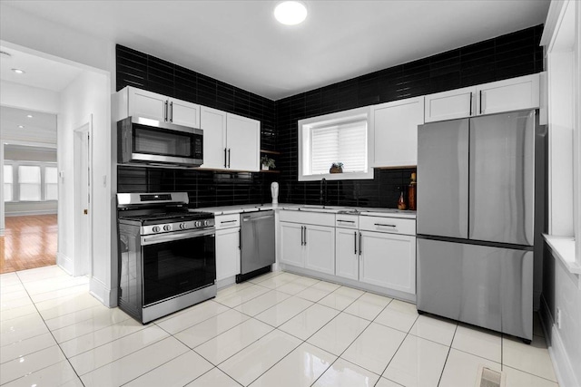 kitchen with decorative backsplash, appliances with stainless steel finishes, light countertops, white cabinets, and a sink