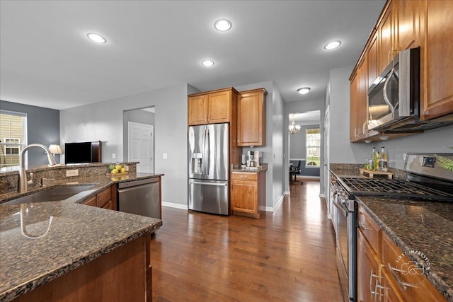 kitchen with brown cabinetry, appliances with stainless steel finishes, dark wood finished floors, a sink, and baseboards