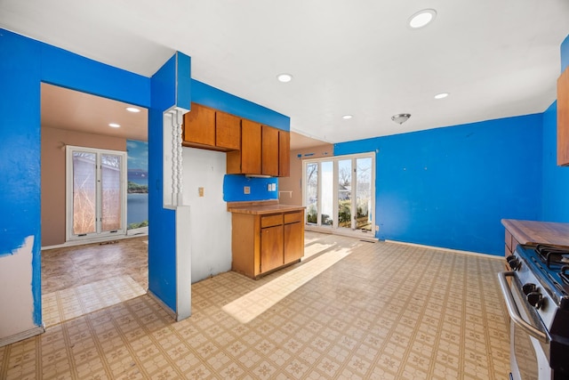 kitchen with recessed lighting, brown cabinetry, stainless steel gas stove, baseboards, and open floor plan