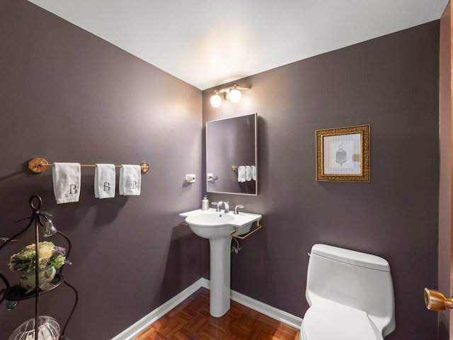 half bath with baseboards, toilet, and a sink