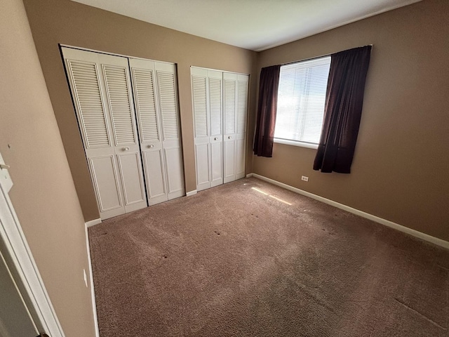 unfurnished bedroom with baseboards, two closets, and carpet
