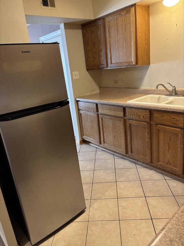 kitchen with a sink, freestanding refrigerator, light countertops, and light tile patterned floors
