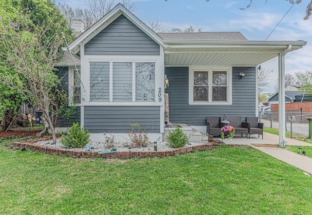 bungalow-style home featuring fence, roof with shingles, a front yard, and an outdoor living space