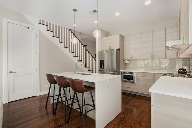 kitchen featuring stainless steel appliances, dark wood-style floors, a sink, a breakfast bar, and light countertops