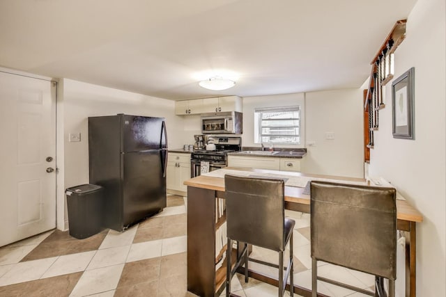 kitchen with a sink, stainless steel appliances, light tile patterned flooring, white cabinetry, and wooden counters