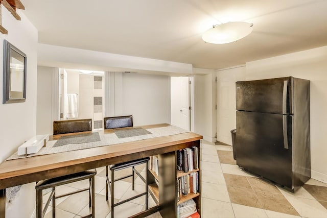 kitchen featuring baseboards, light tile patterned flooring, and freestanding refrigerator