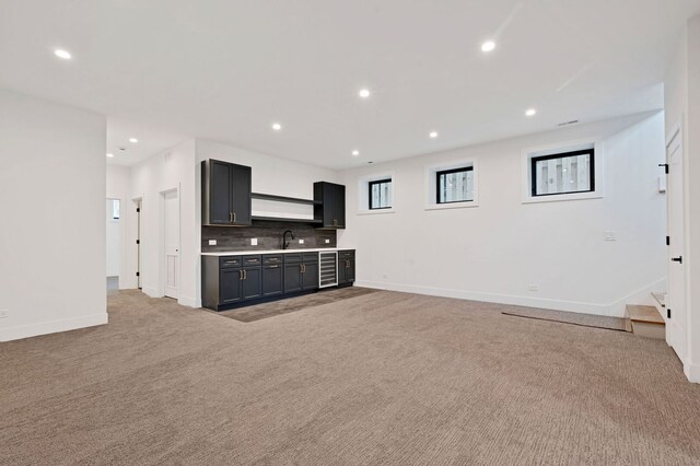 unfurnished living room with a sink, baseboards, light carpet, and recessed lighting