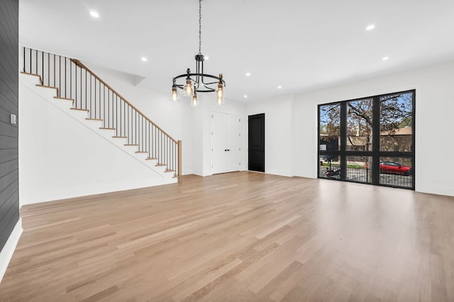 unfurnished living room with light wood-style floors, an inviting chandelier, stairway, and recessed lighting