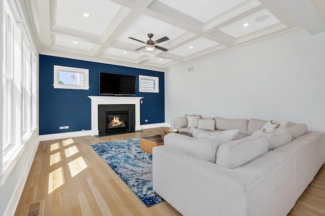 living room featuring coffered ceiling, beam ceiling, a fireplace with flush hearth, a ceiling fan, and light wood-type flooring