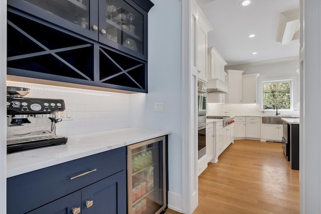 bar with wine cooler, tasteful backsplash, light wood finished floors, recessed lighting, and a sink