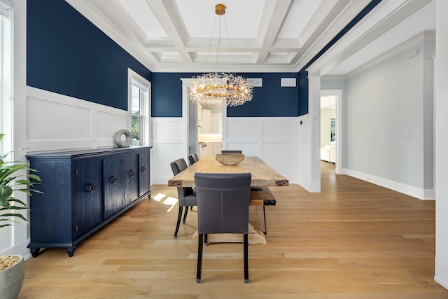 dining space with a chandelier, a decorative wall, coffered ceiling, light wood finished floors, and a wainscoted wall