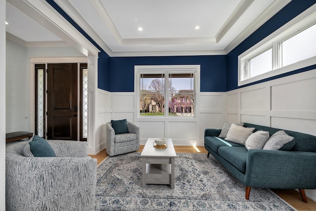 living room with a raised ceiling, a decorative wall, wood finished floors, and wainscoting