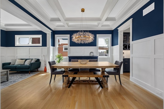 dining space with a decorative wall, a chandelier, coffered ceiling, a wainscoted wall, and light wood-style floors