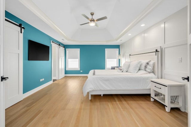 bedroom featuring a barn door, a tray ceiling, light wood-style floors, a ceiling fan, and recessed lighting