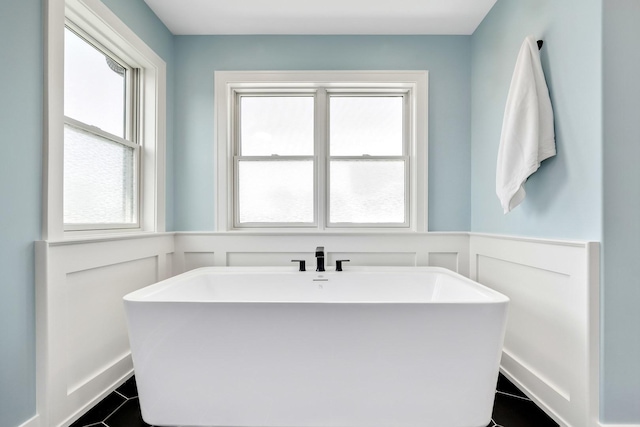 bathroom with a decorative wall, a wainscoted wall, a freestanding tub, and tile patterned floors