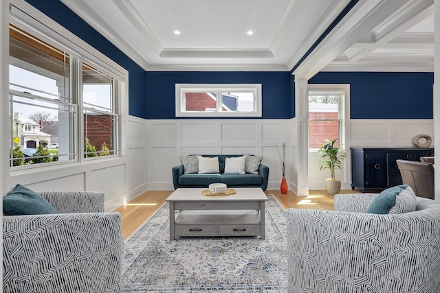 living area featuring a decorative wall, wood finished floors, wainscoting, and crown molding