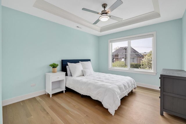 bedroom featuring a raised ceiling, light wood-style floors, baseboards, and a ceiling fan
