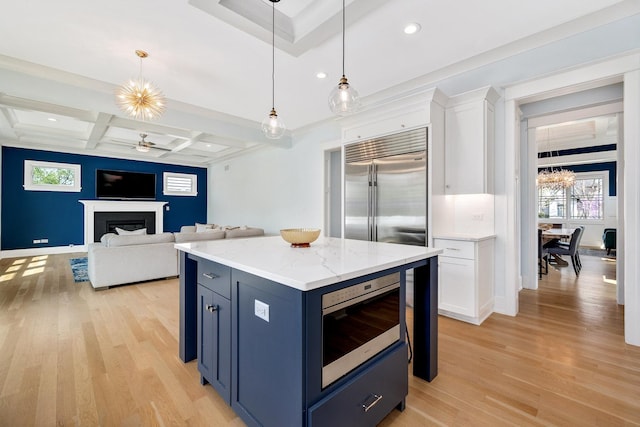 kitchen featuring a fireplace, built in appliances, plenty of natural light, white cabinets, and coffered ceiling