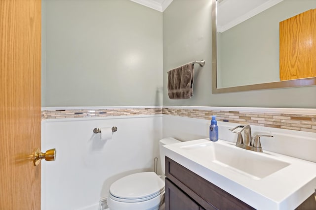 half bath featuring toilet, ornamental molding, tile walls, vanity, and wainscoting