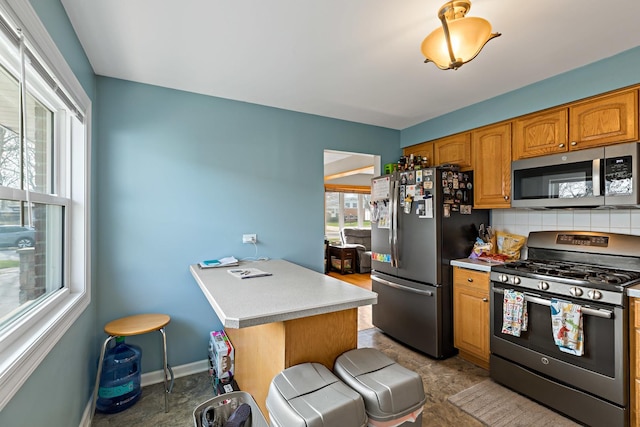 kitchen featuring brown cabinets, light countertops, tasteful backsplash, baseboards, and appliances with stainless steel finishes