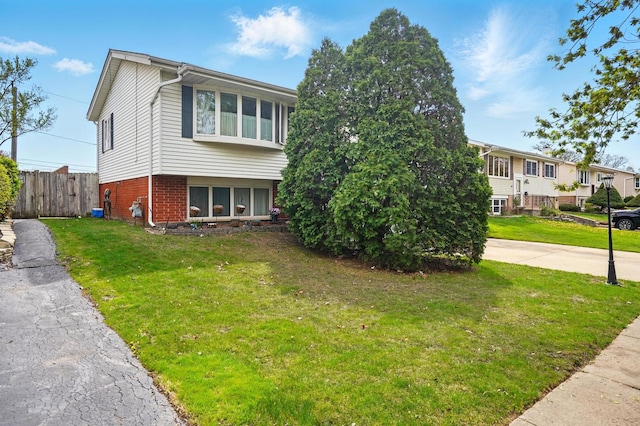 view of front of property with brick siding, fence, driveway, and a front yard