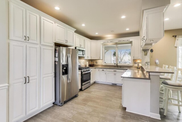 2502 S Hidden Trl, Spring Grove, IL 60081 - kitchen featuring a breakfast bar, a sink, white cabinetry, a peninsula, and appliances with stainless steel finishes