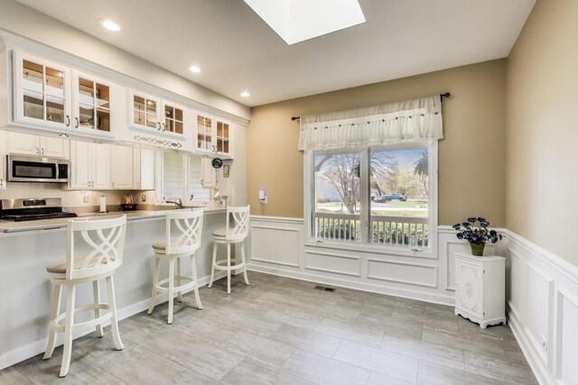 2502 S Hidden Trl, Spring Grove, IL 60081 - kitchen with glass insert cabinets, a kitchen bar, stainless steel appliances, visible vents, and wainscoting