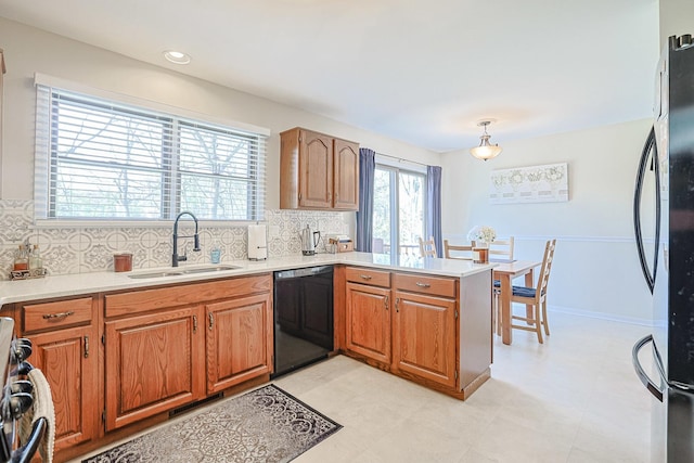 kitchen with a sink, black dishwasher, a peninsula, freestanding refrigerator, and backsplash