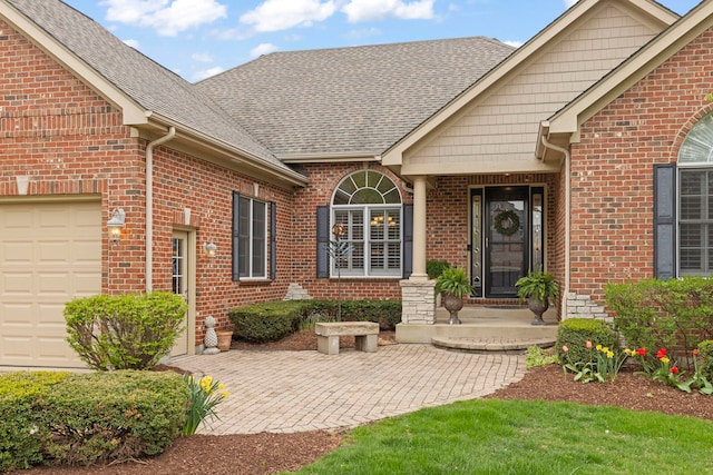 doorway to property with brick siding, an attached garage, and a shingled roof