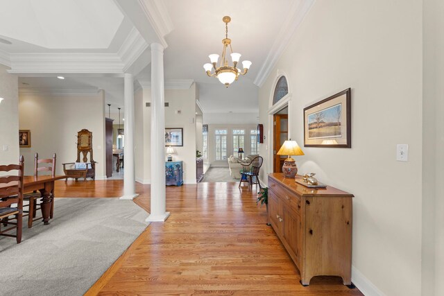 entryway with decorative columns, crown molding, light wood-type flooring, a chandelier, and baseboards