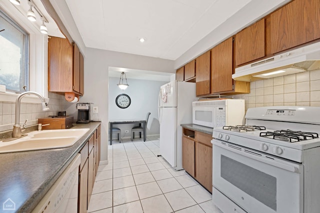 kitchen featuring decorative backsplash, a sink, under cabinet range hood, light tile patterned flooring, and white appliances