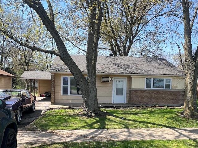 single story home featuring brick siding, a carport, a front yard, and roof with shingles