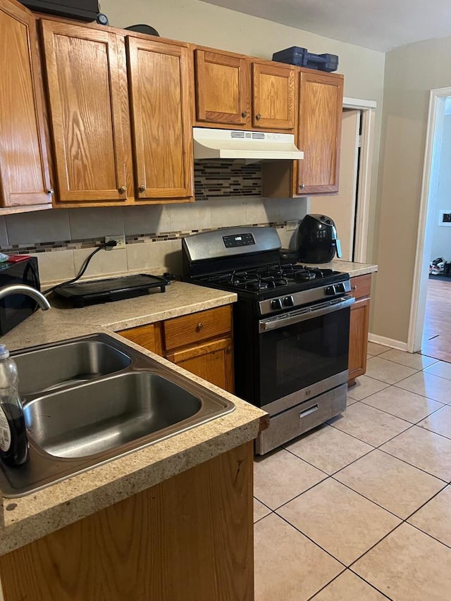 kitchen featuring stainless steel gas range, under cabinet range hood, tasteful backsplash, and light tile patterned floors