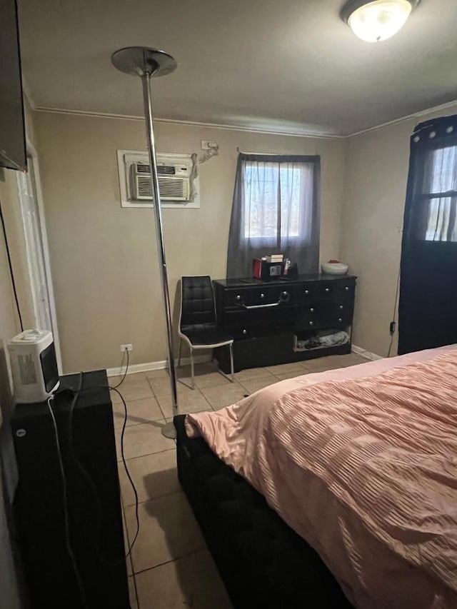 bedroom featuring an AC wall unit, light tile patterned floors, crown molding, and baseboards