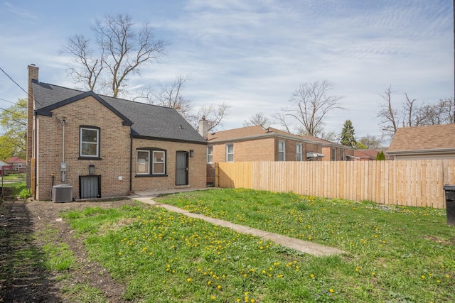 back of property featuring brick siding, fence, a yard, and a chimney