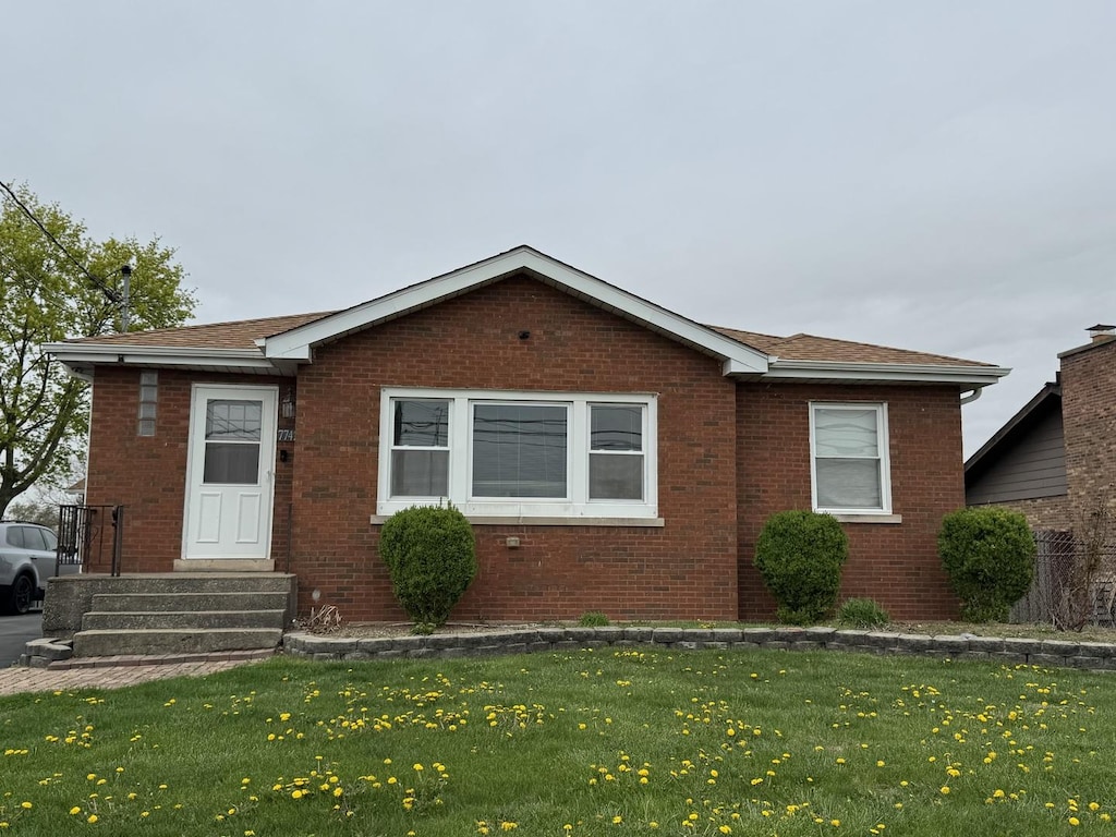 view of front of property with brick siding, a shingled roof, and a front yard