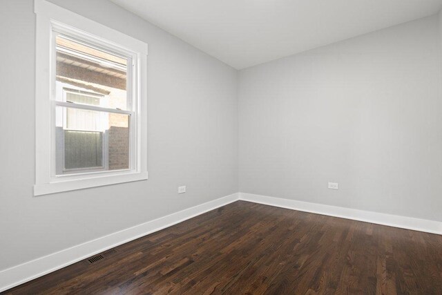 empty room with dark wood-style flooring, visible vents, and baseboards